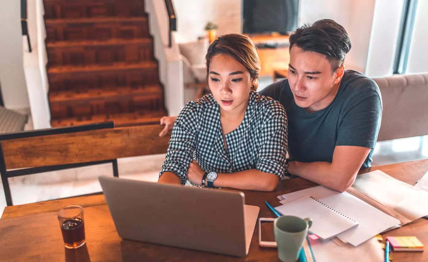  A young couple reviews financial information on their laptop, with notebooks spread out in front of them.
