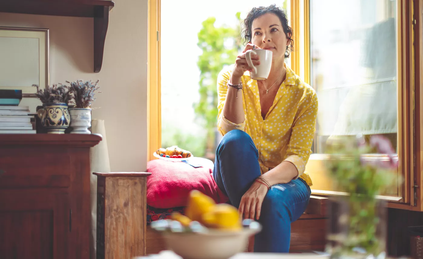  A person seated in front of a window, sipping coffee in deep contemplation.

