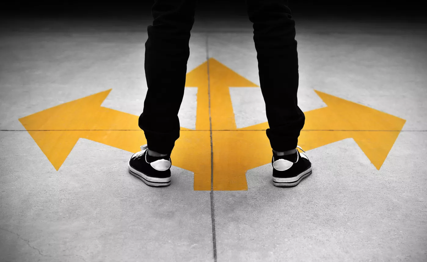  Person standing on a sidewalk painted with arrows pointing in different directions.
