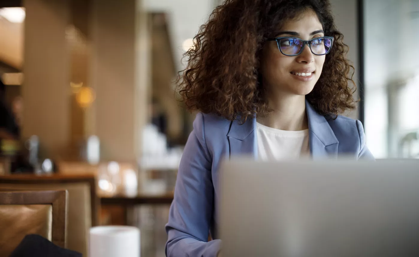  A professional woman looks at her open laptop in a cafe with a cup of coffee next to her.
