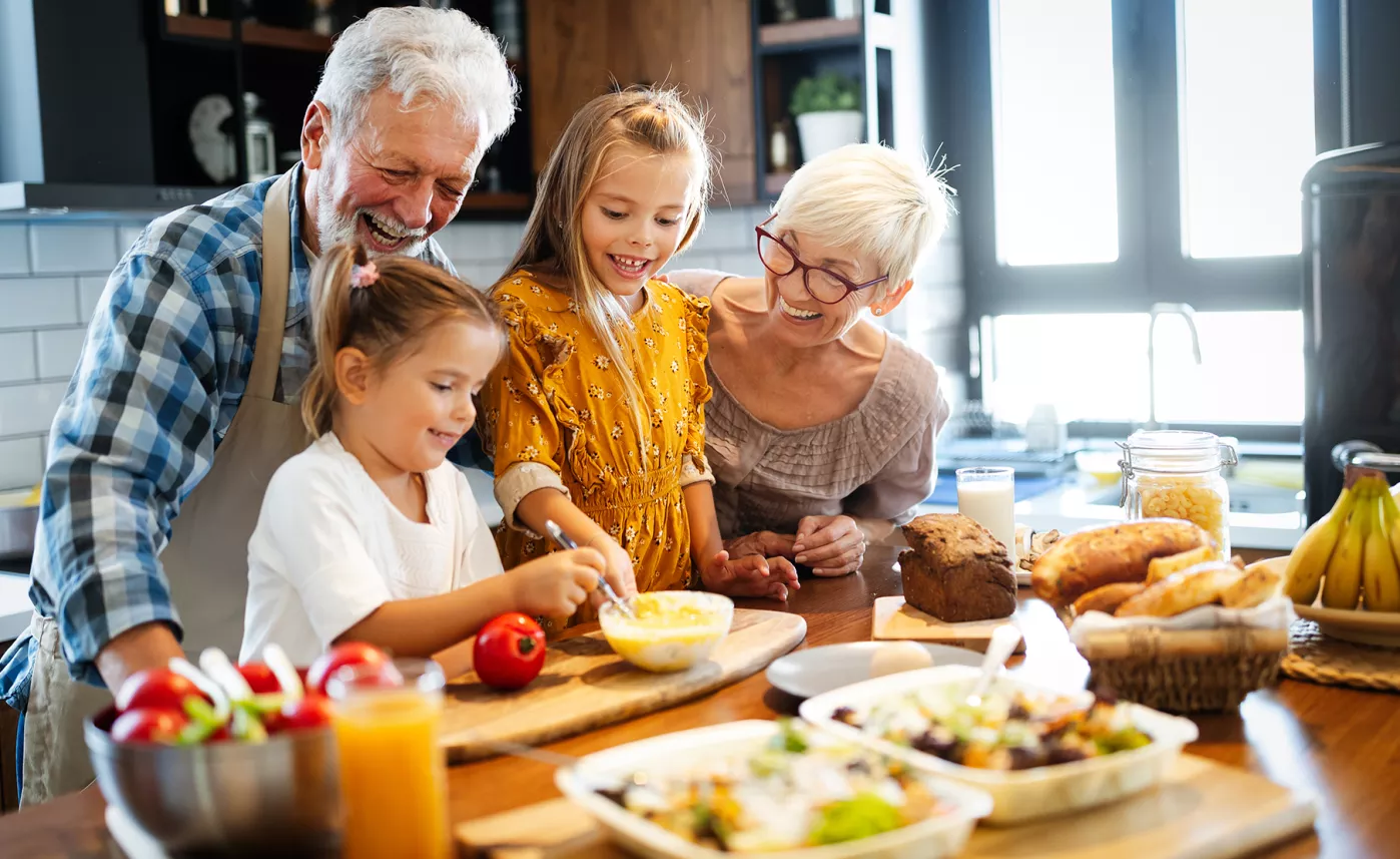  Two grandparents cook in their kitchen with their young grandchildren.
