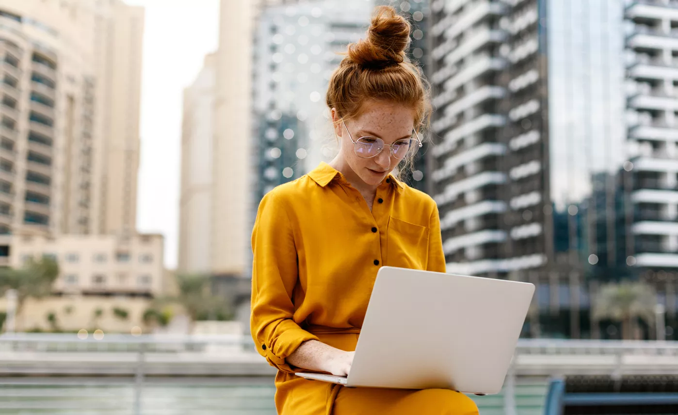  A young woman works on her laptop while sitting outside in an urban area.
