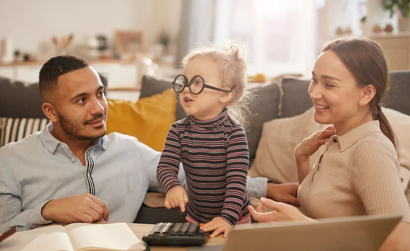  Young parents sit with their toddler daughter as she playfully taps on a calculator.
