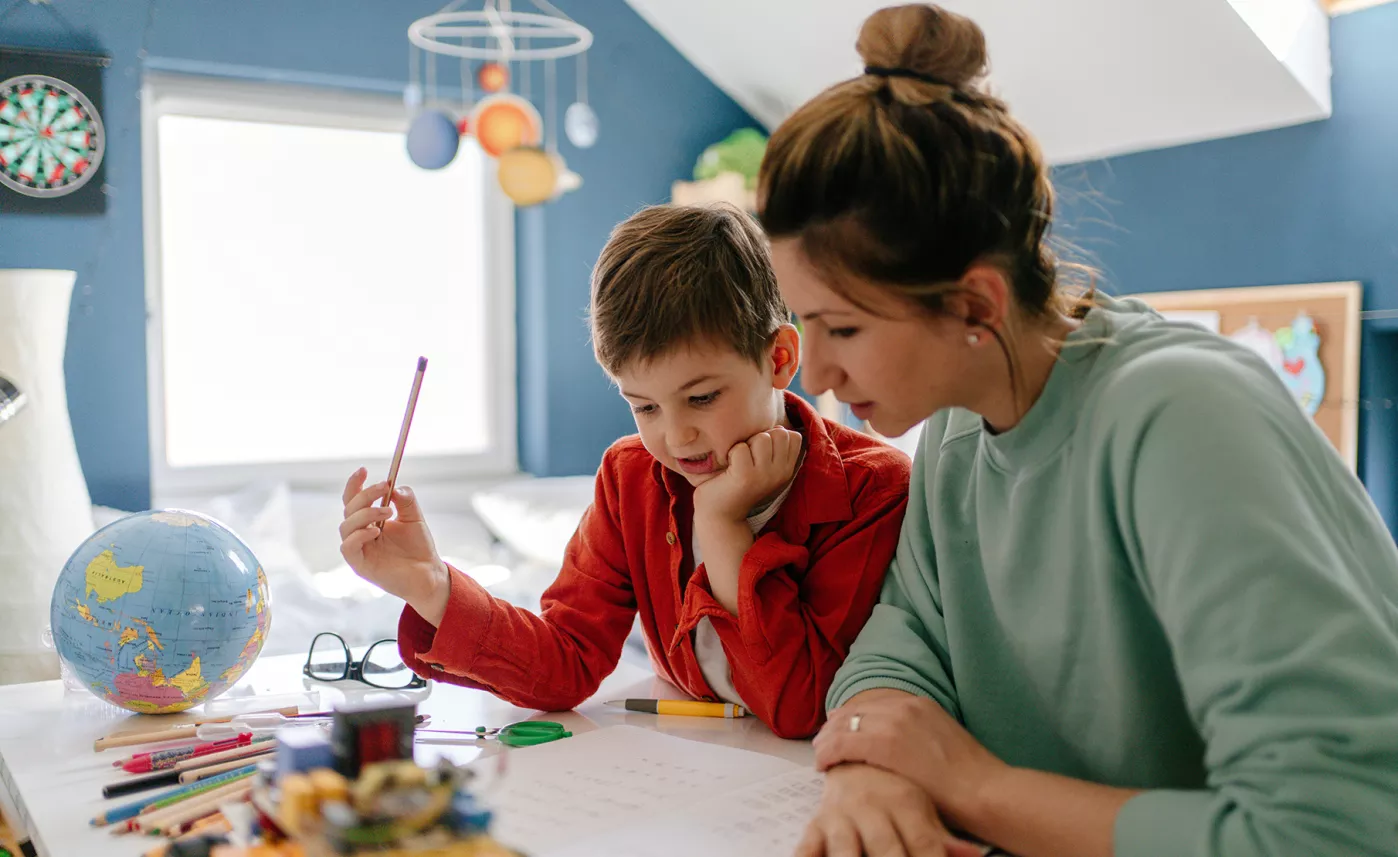  A mother and her young child work on his homework together in his bedroom.
