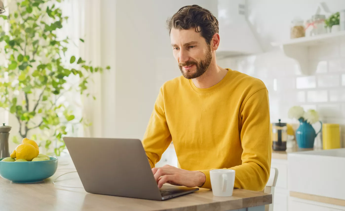 A man views tax forms on his laptop at his kitchen table.
