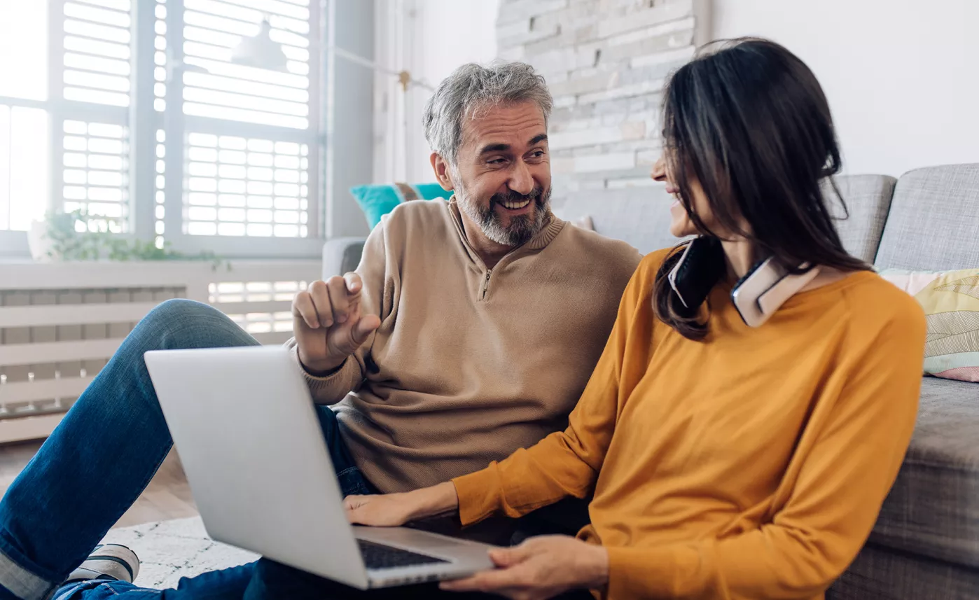  A couple smiles at each other while they do their taxes together in the living room.

