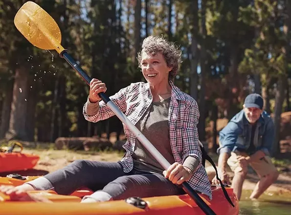  A retirement-aged woman kayaks in a lake with her husband on a sunny day.
