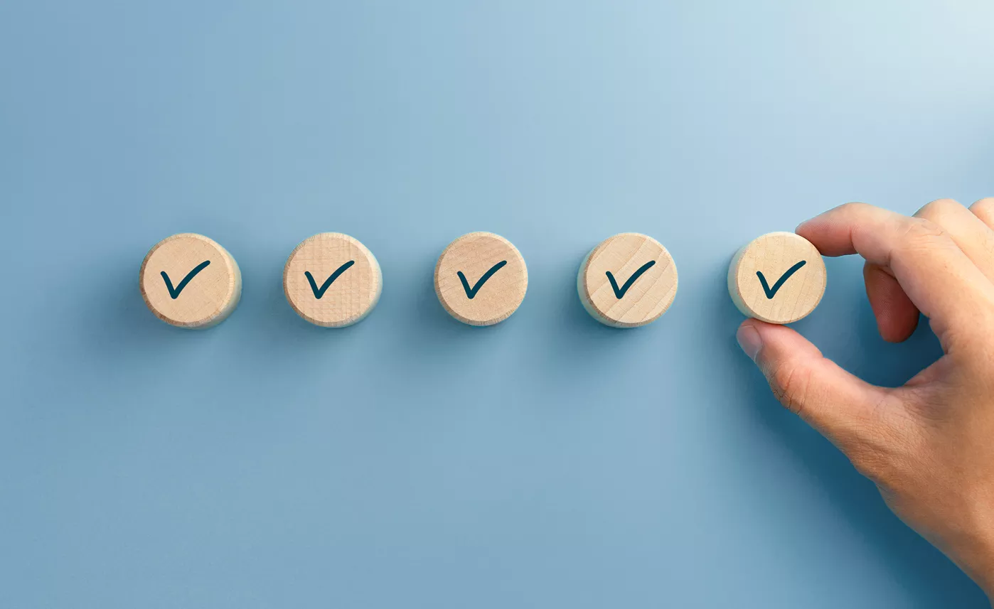  A person's hands placing a wooden checkmark at the end of a row of wooden checkmarks.
