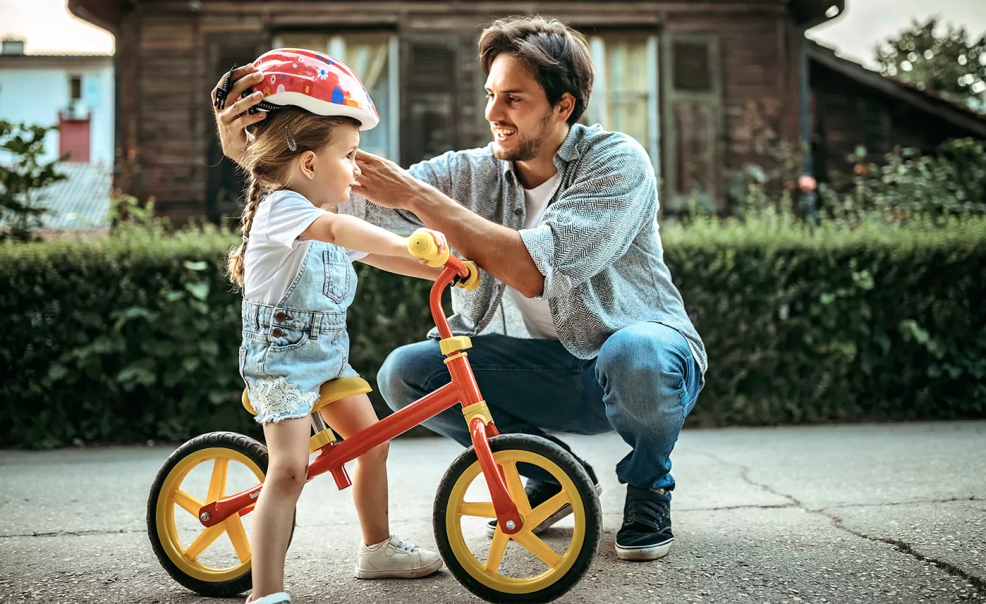  A parent putting a helmet on their young child who is sitting on a bike.
