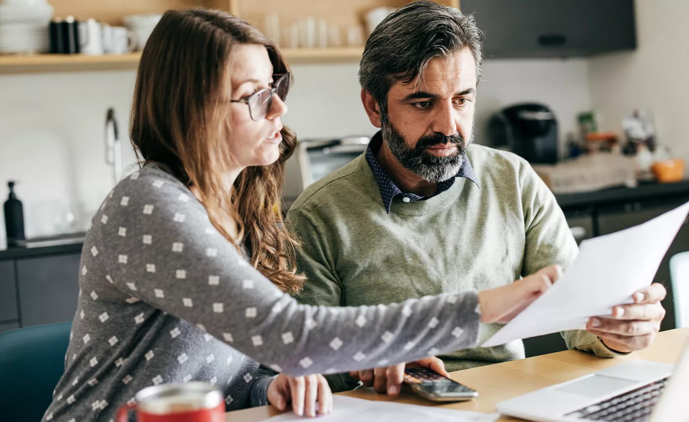  A couple sitting at a kitchen table, looking at a document together.
