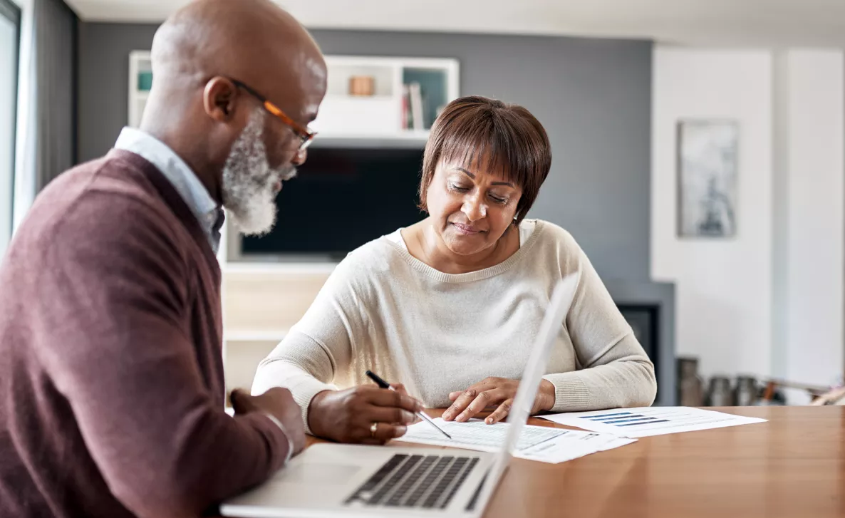  A couple looks over documents with financial information with their laptop open.
