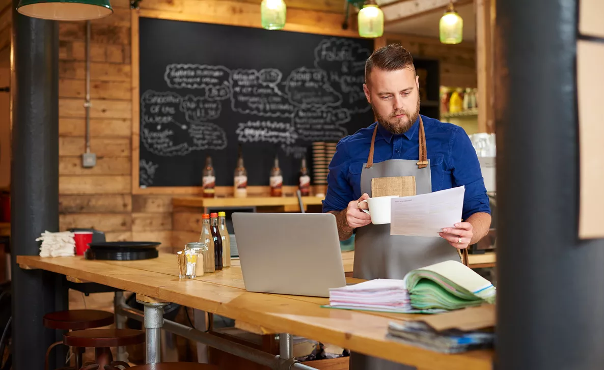  A young business owner review financial documents in his cafe with a cup of coffee.
