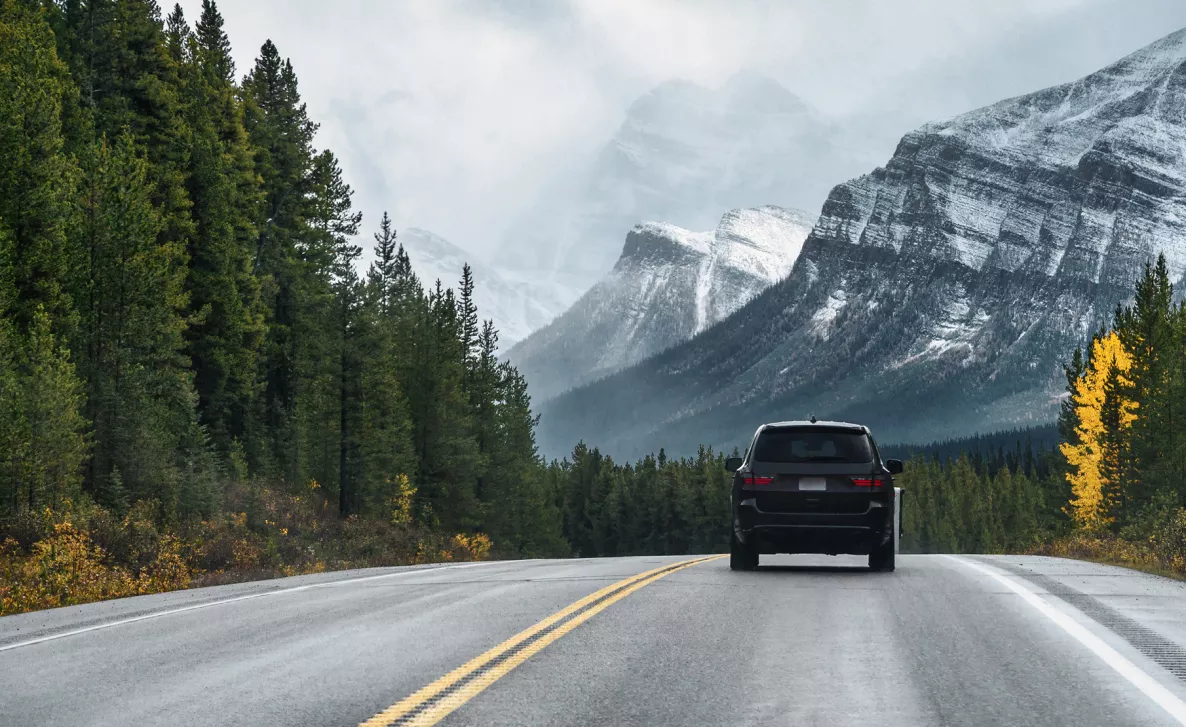 A car driving on a highway with trees and mountains in background
