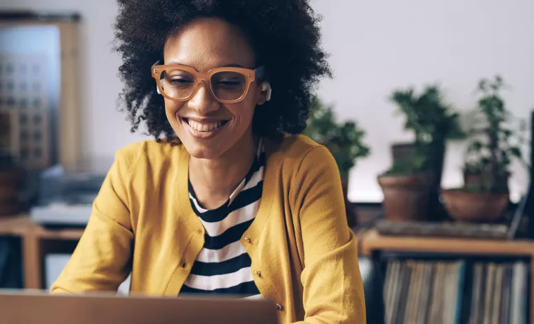 A woman smiles as she pays bills on her laptop in her home office.