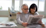 A woman reads a newspaper with her father.