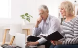 A couple sitting and reviewing information on a laptop and in a notebook..