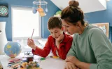 A mother and her young child work on his homework together in his bedroom.