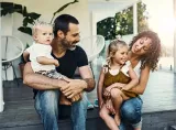 A young family – father, mother, and two young children – sits on their porch and laughs together.