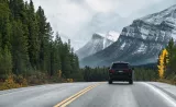 A car driving on a highway with trees and mountains in background