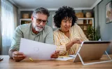 A couple reviewing paper documents together while looking at a tablet.