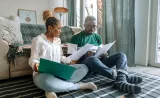 A couple happily smiling and looking at papers together.