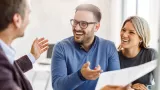 Two people smile and point to a paper while looking at another person